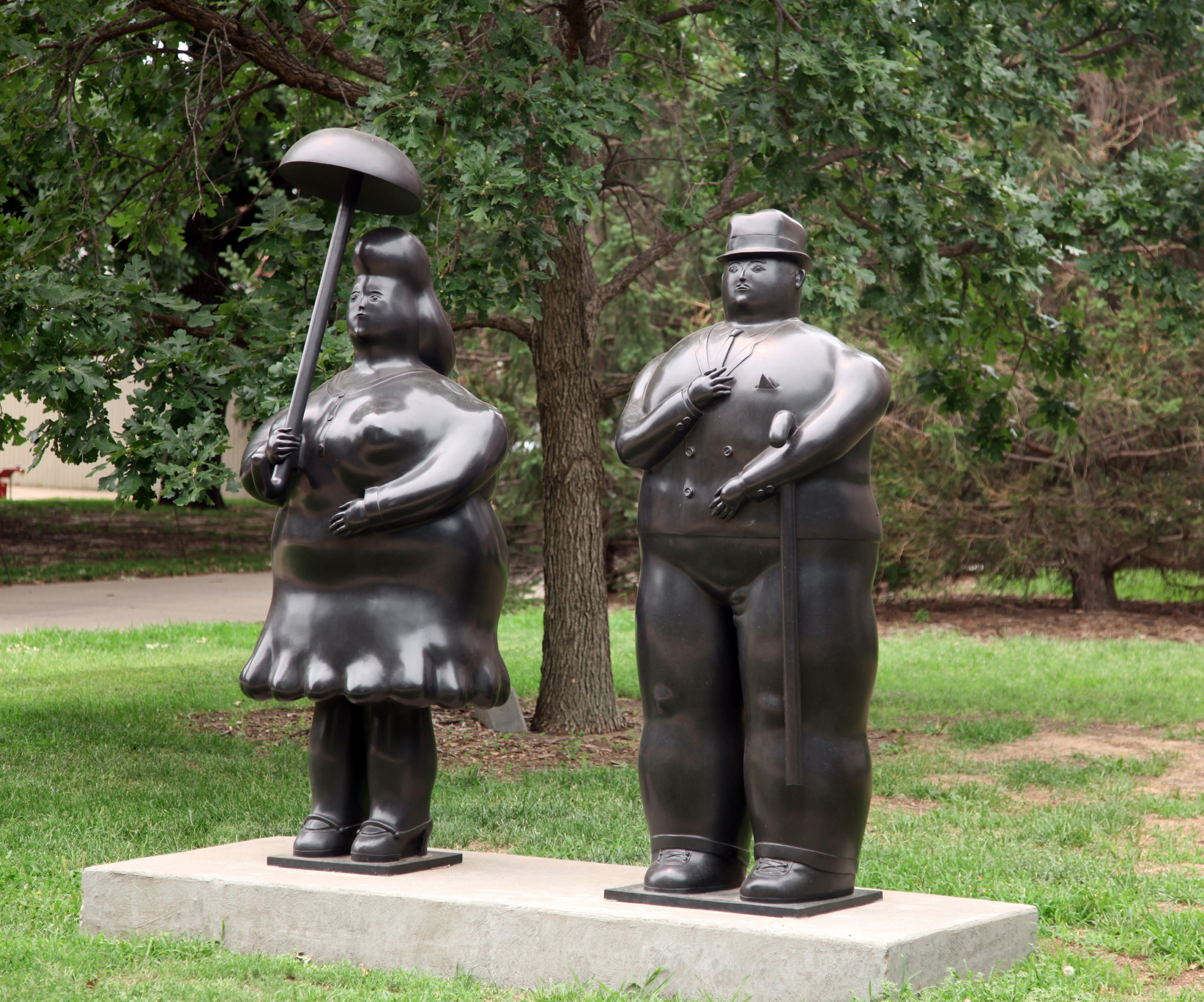 Two large statues, one of a woman with an umbrella, and the other of a man with a cane stand next to eachother