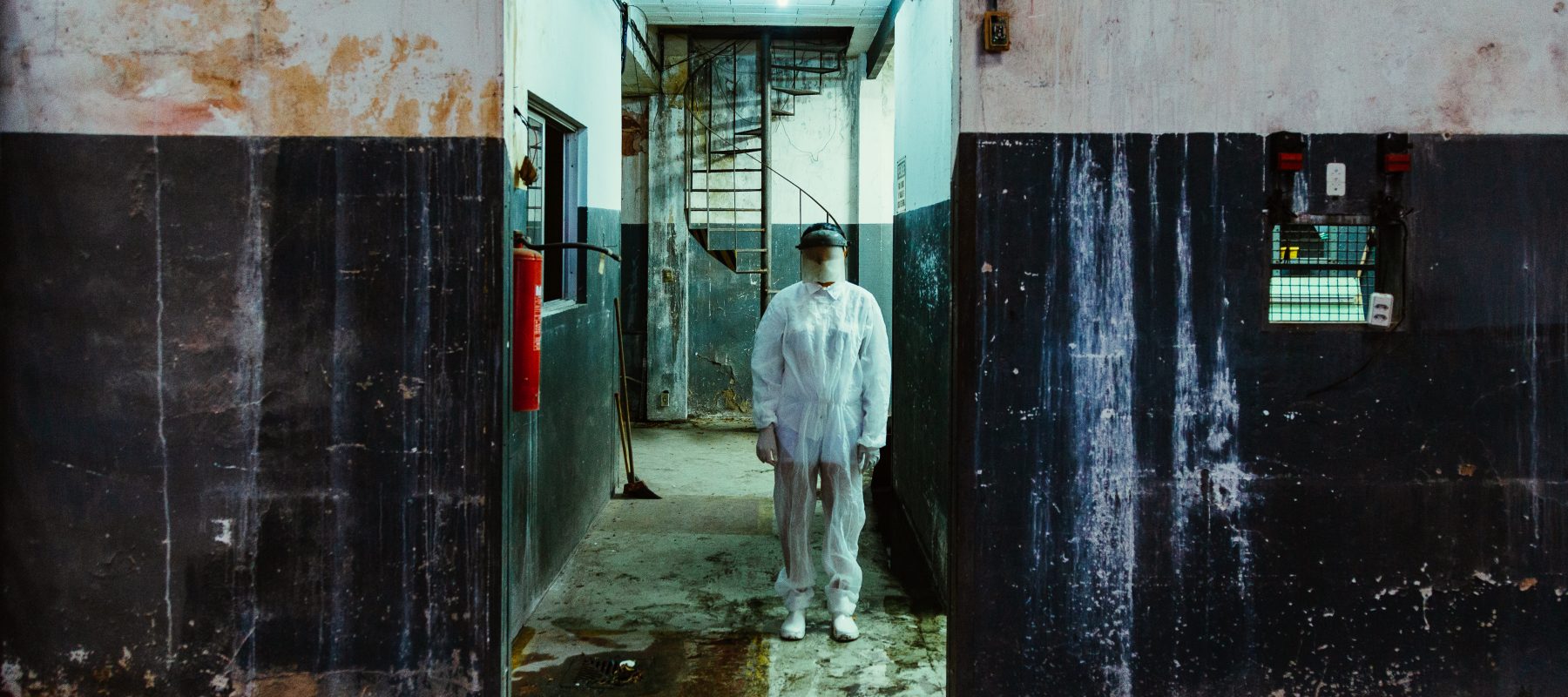 A person stands shrouded in an industrial setting that looks dirty and wet.
