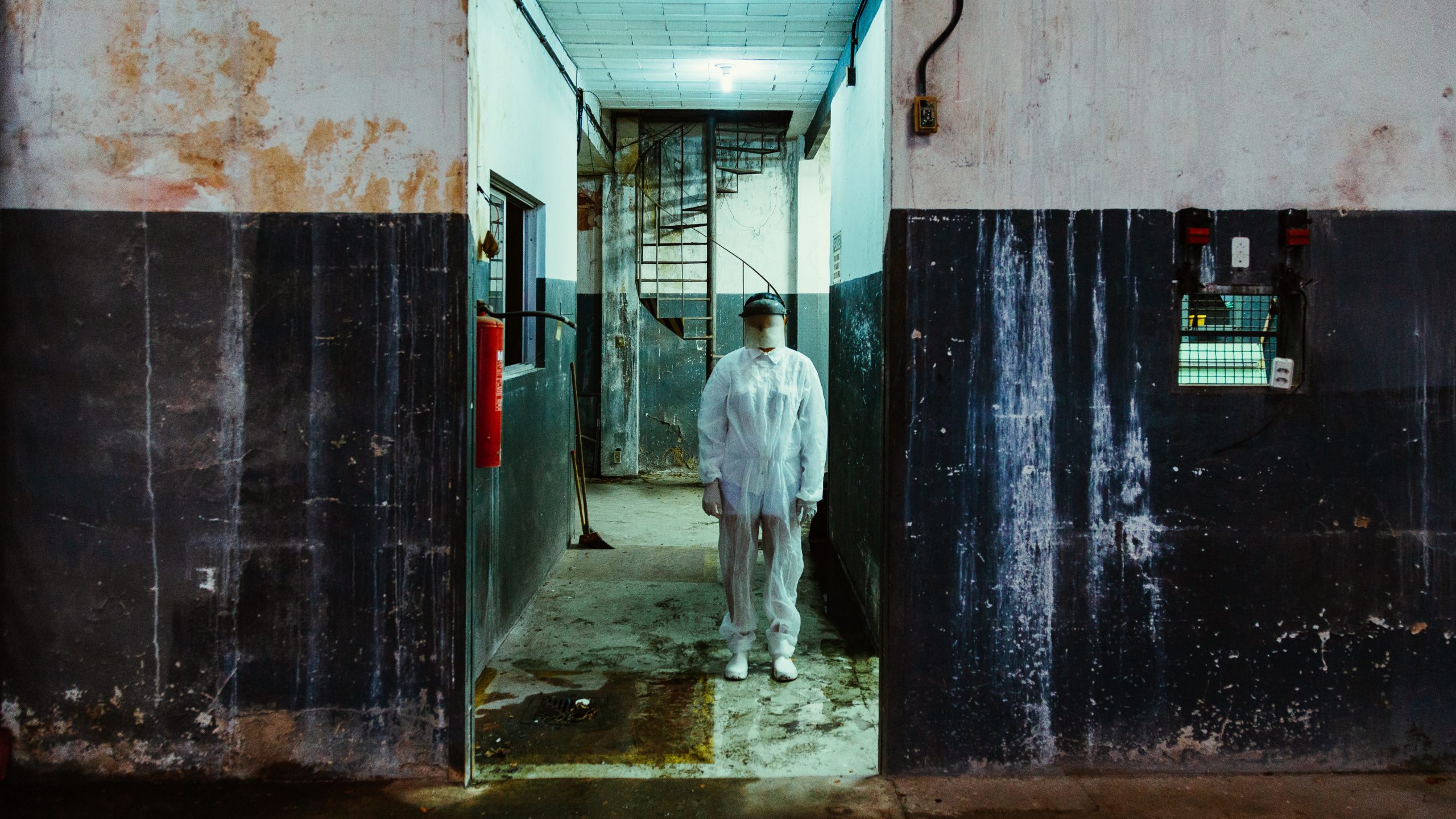 A person stands shrouded in an industrial setting that looks dirty and wet.
