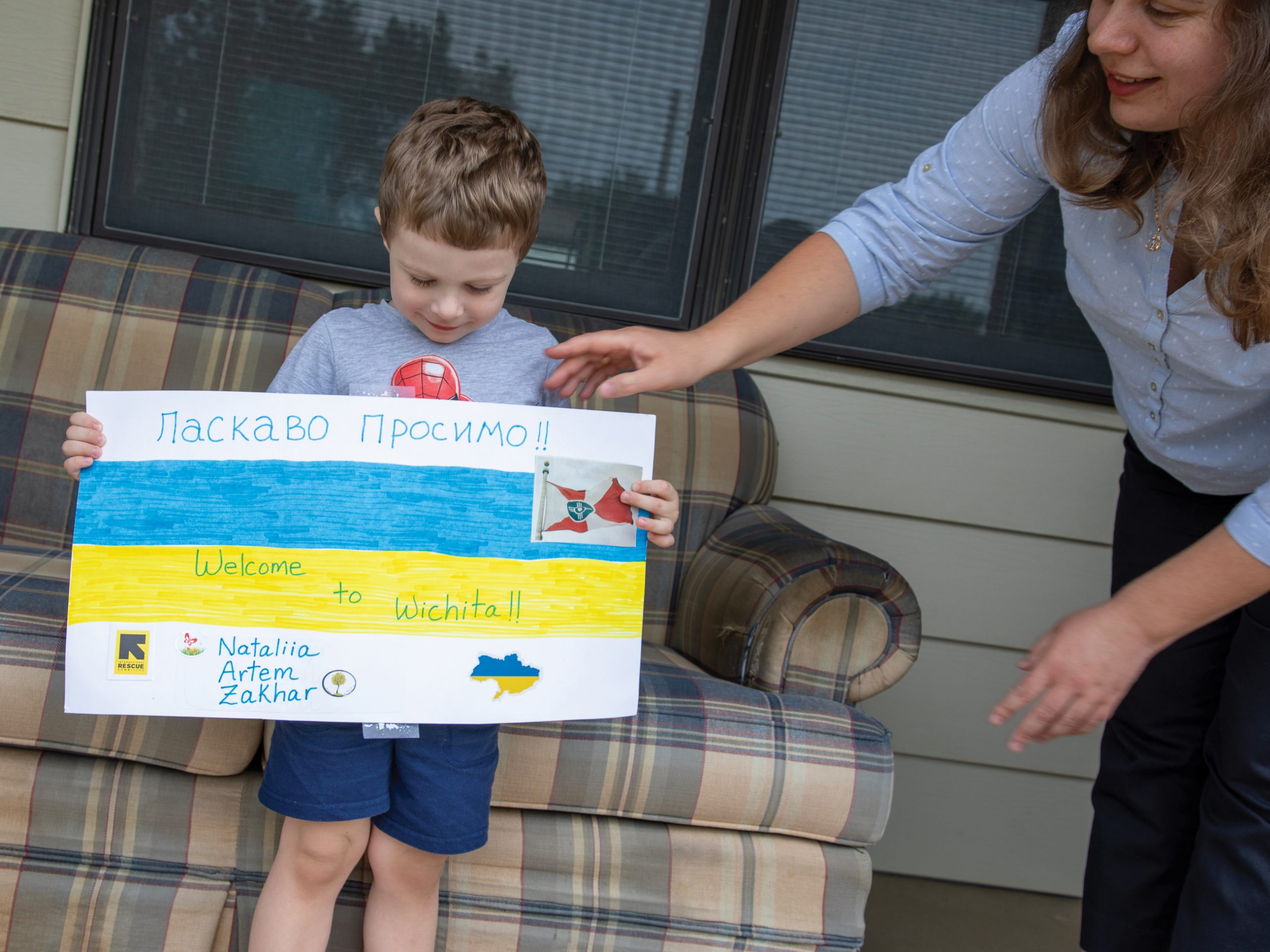 A boy with a poster board that has the Ukrainian flag and the words welcome to Wichita along with Ukrainian writing.