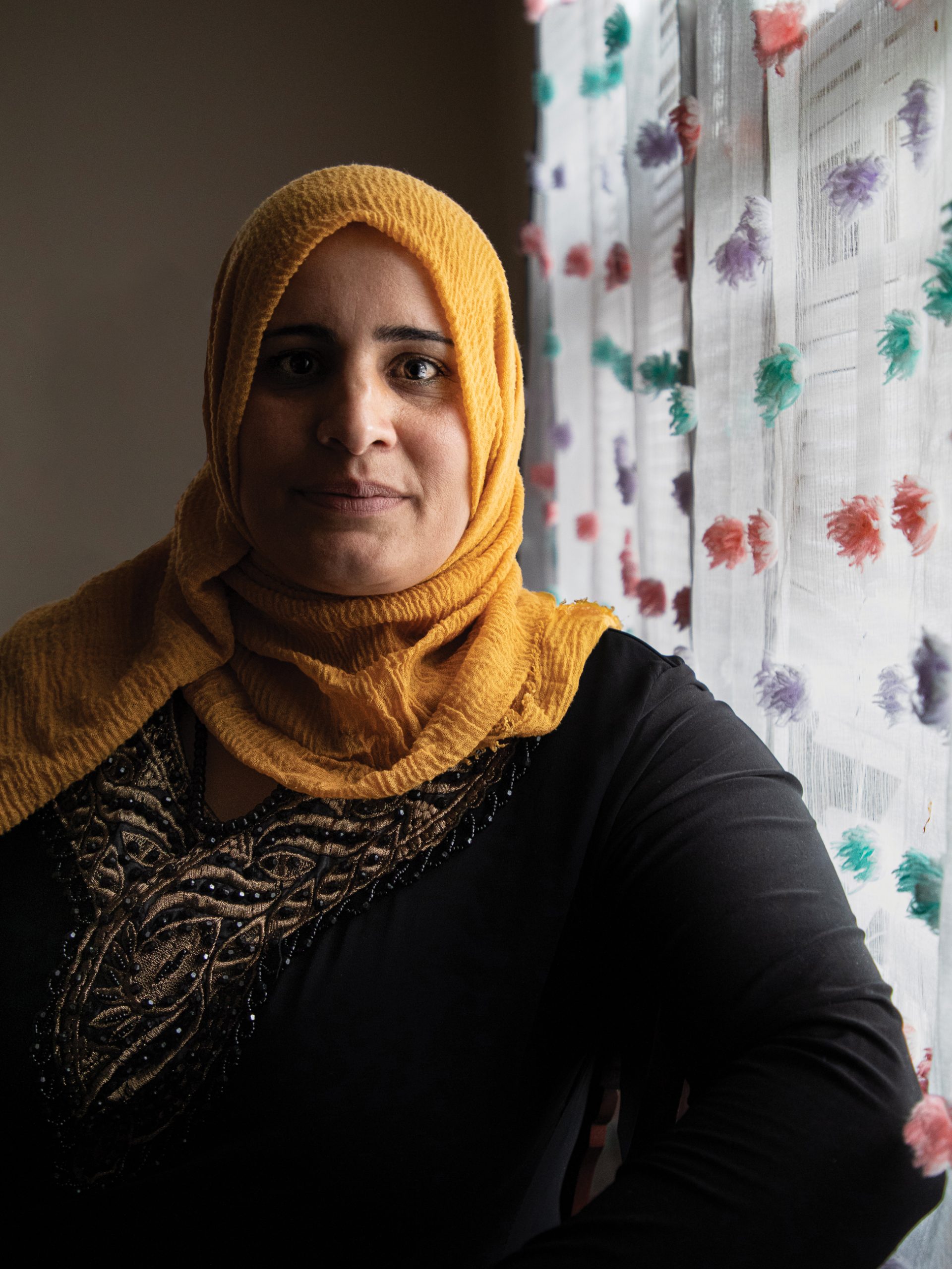Woman with head covering standing next to a window