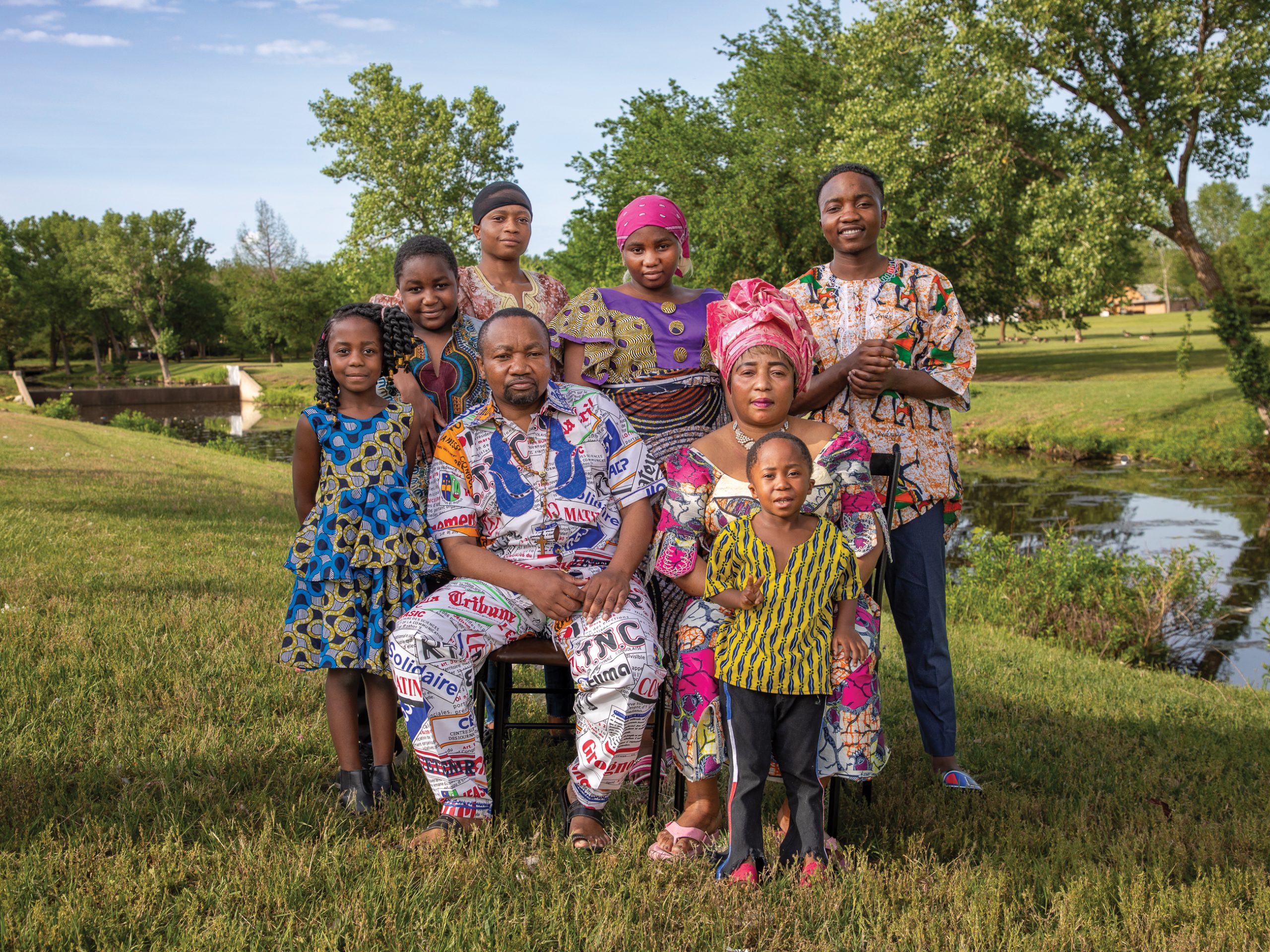 A family of eight sit for a portrait in Congolese clothing in a field near a stream