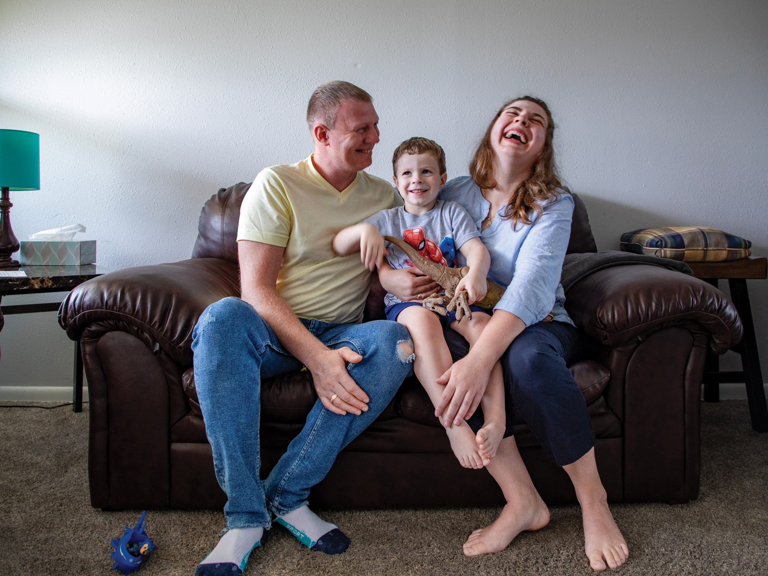 A man and woman sit with their son on a couch, laughing