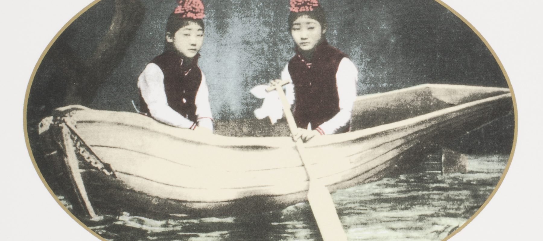 Two women in red hats are rowing a boat.