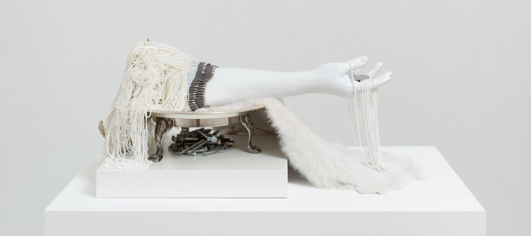 A white artwork featuring an arm, feathers, and beadwork.